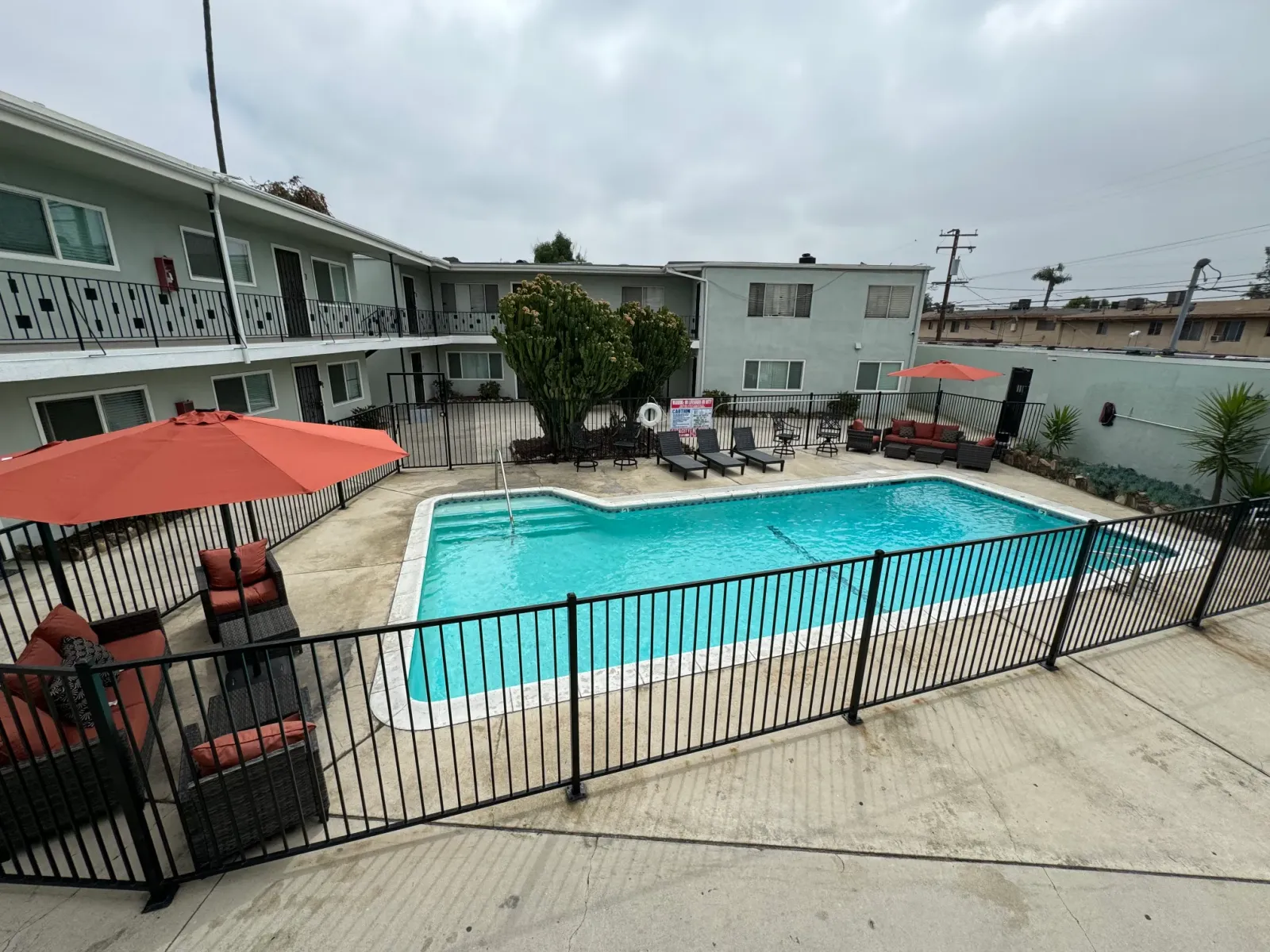 Fenced swimming pool with red umbrellas and patio seating